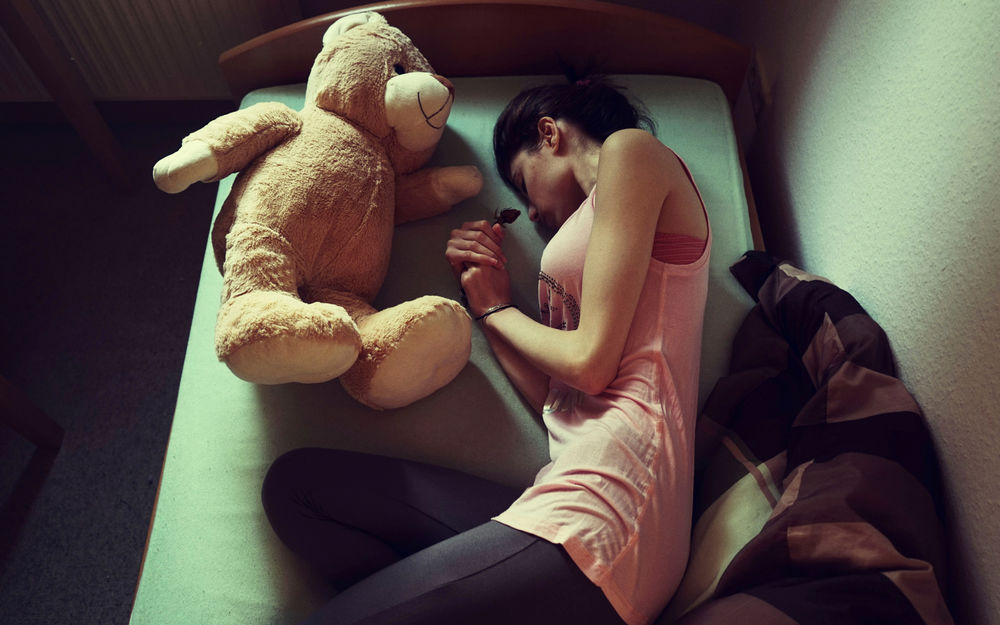 Обои для рабочего стола Девушка с игрушечным медведем лежит на кровати