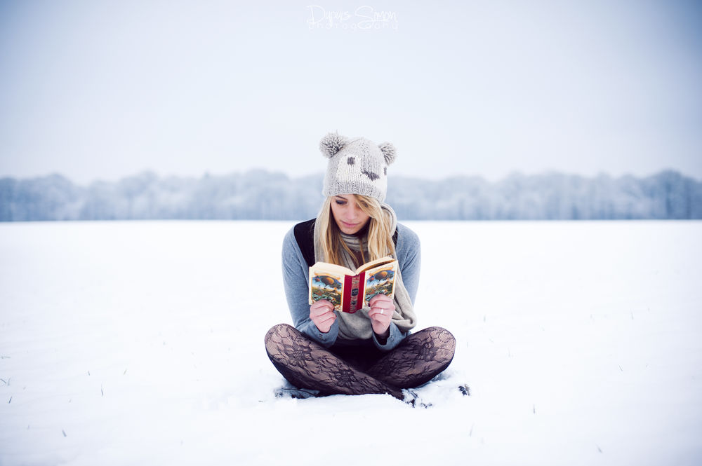 Обои для рабочего стола Девушка читает книгу, сидя на снегу