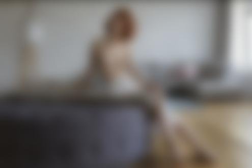 Обои для рабочего стола Стройная рыжеволосая девушка в белой юбке топлес позирует, сидя на пуфе в комнате. Фотограф Вячеслав Щербаков