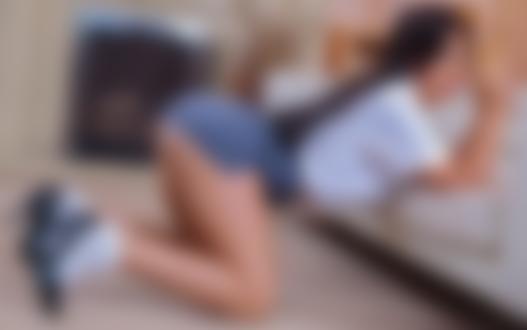 Обои для рабочего стола Девушка в короткой юбке и кофте позирует у камина, облокотившись на диван