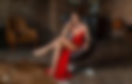 Обои для рабочего стола Модель Ирина с украшением на шее, в красном длинном платье позирует, сидя на кресле в комнате. Фотограф Михаил Герасимов