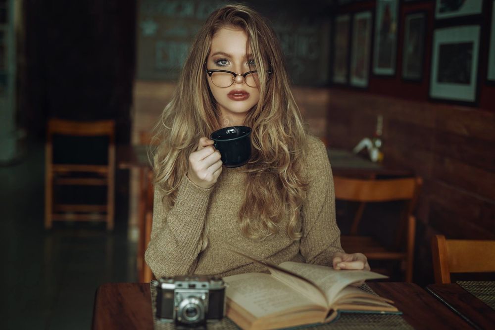 Обои для рабочего стола Девушка в очках, с чашкой в руке, сидит за столом. Фотограф Thiago Bomfim
