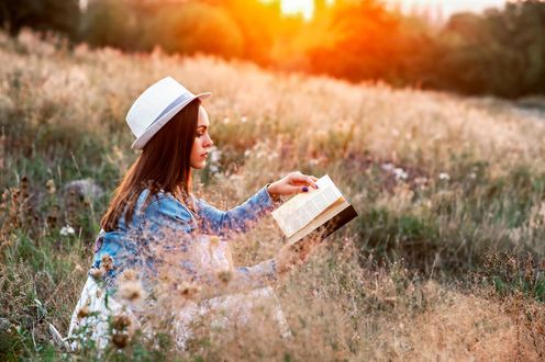 Обои на рабочий стол Девушка в шляпе с книгой в руках сидит в траве
