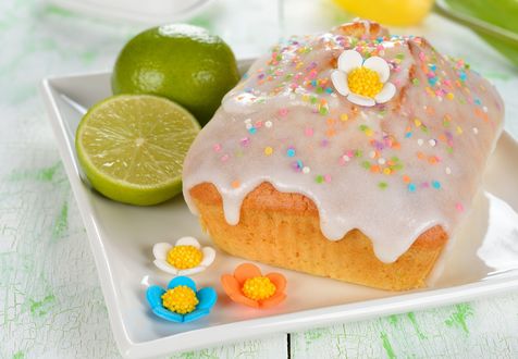 Обои на рабочий стол Пасхальный кулич, покрытый сахарной глазурью и украшенный марципановыми цветочками, с половинками лайма на белой подставке