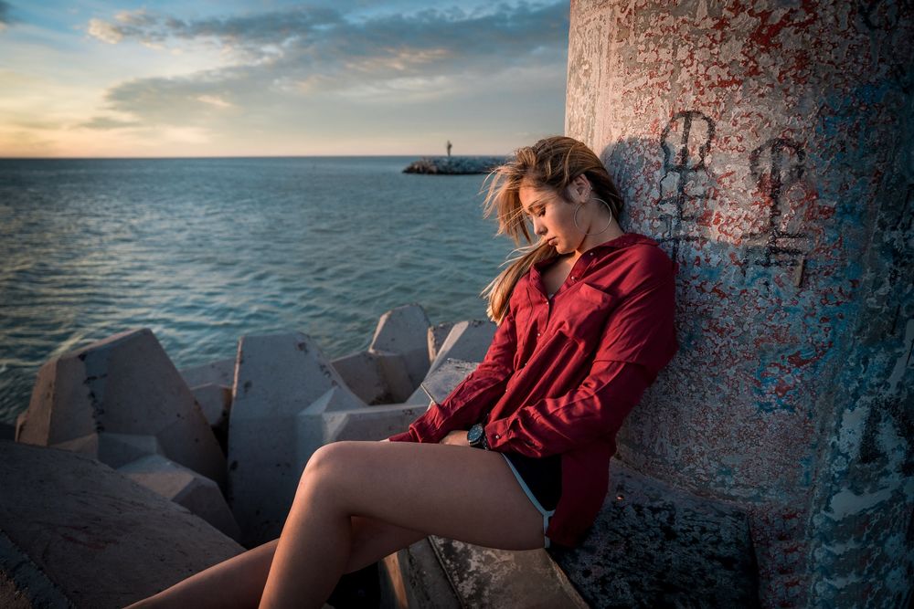 Обои для рабочего стола Модель Paulina / Паулина в красной рубашке сидит у бетонной колонны на фоне моря