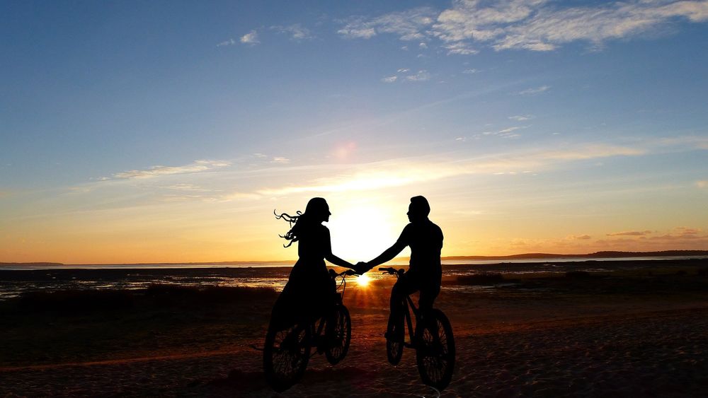 Обои для рабочего стола Парень с девушкой на велосипедах стоят на фоне заката солнца