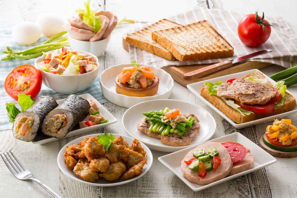 Обои для рабочего стола Вкусный завтрак: тосты, роллы, мясная нарезка, яйца, спаржа, овощной салат и помидор на столе