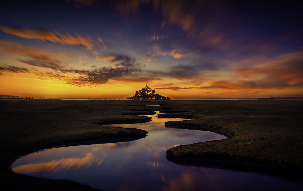 Обои для рабочего стола Извилистая река перед островом-крепостью Mont Saint-Michel / Мон-Сен-Мишель, France / Франция на фоне неба во время заката. Фотограф Hmetosche Saidani