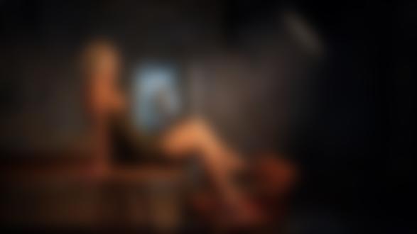 Обои для рабочего стола Модель Жанна в приспущенном платье с обнаженной грудью сидит на столе в комнате на фоне стены с зеркалом, фотограф Георгий Чернядьев
