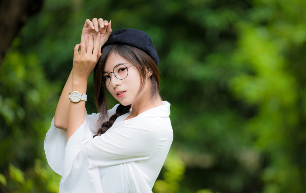 Обои для рабочего стола Азиатка в очках в берете и белой блузке позирует на фоне природы