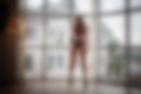 Обои для рабочего стола Длинноволосая блондинка в черных трусиках стоит в комнате спиной к камере у окна с видом на городские дома, фотограф Олег Коваленко