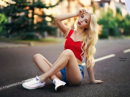 Обои на рабочий стол Модель Ульяна Веренчикова в красном топе и в джинсовых шортах сидит на дороге на размытом фоне деревьев и здания, фотограф Alex Мarti