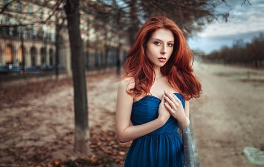 Обои на рабочий стол Рыжеволосая девушка в синем платье стоит на дороге на фоне деревьев и городского здания
