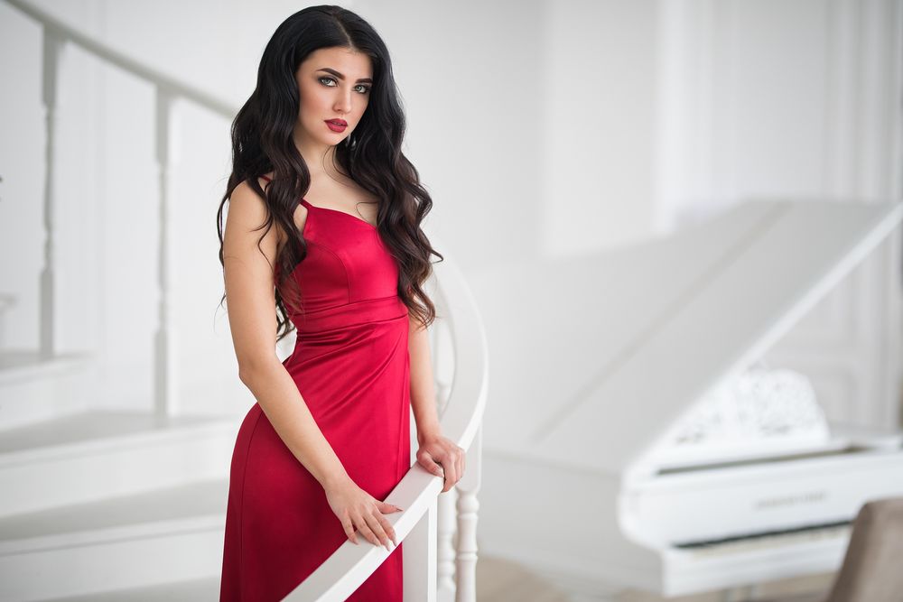 Обои для рабочего стола Модель Кристина Романова в красном платье стоит на лестнице, в комнате с белым роялем, фотограф Дмитрий Шульгин