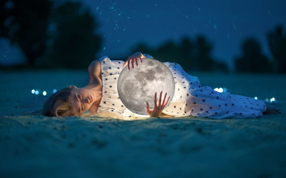 Обои для рабочего стола Молодая девушка с луной в руках лежит на песке
