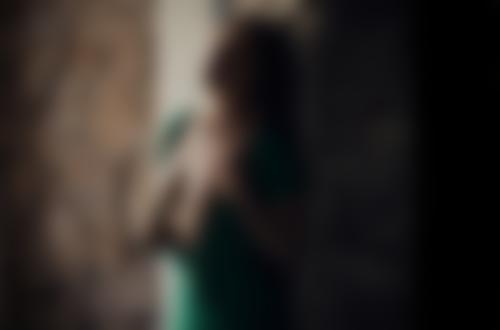 Обои для рабочего стола Девушка с закрытыми глазами в расстегнутом зеленом платье с обнаженной грудью стоит у кирпичной стены