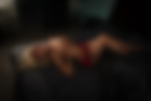 Обои на рабочий стол Блондинка с тату на ноге в приспущенном красном нижнем белье лежит на кровати в комнате, прикрывая руками грудь