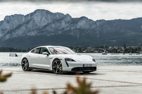 Обои на рабочий стол Белый Porsche Taycan Turbo S 2019 стоит на побережье с видом на поселок у подножья скал