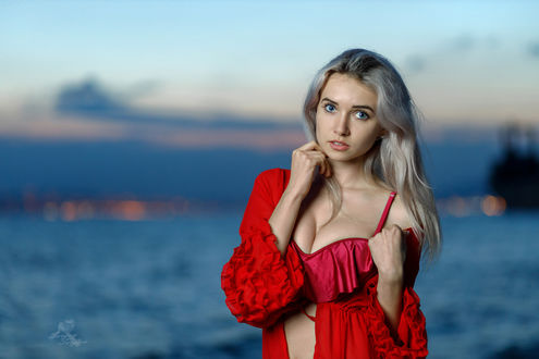 Обои на рабочий стол Девушка - блондинка в красном стоит на фоне воды, фотограф Sergey Sergeev