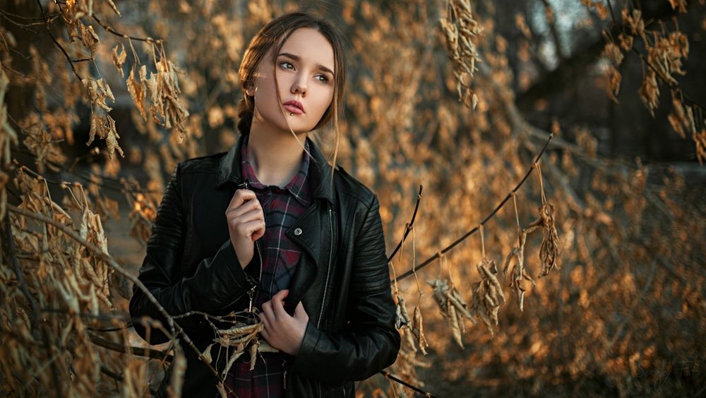 Обои для рабочего стола Модель Лада Чернышева в черной кожанке стоит на фоне ветвей деревьев с засохшей листвой, фотограф Сергей Жирнов