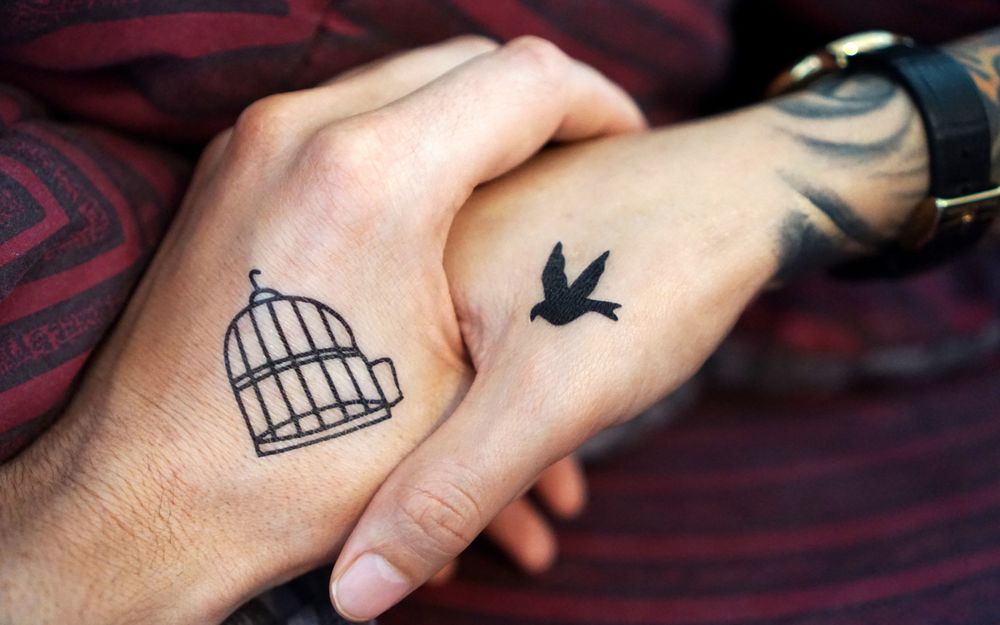 Обои для рабочего стола Мужская рука с тату клетки держит женскую руку с тату птицы