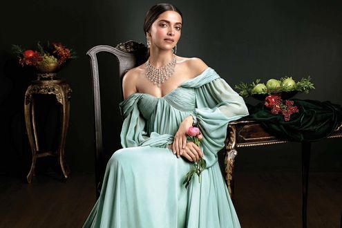 Обои на рабочий стол Актриса Дипика Падуконе в шикарном платье, с оголенными плечами и с украшением на шее сидит у стола с цветами