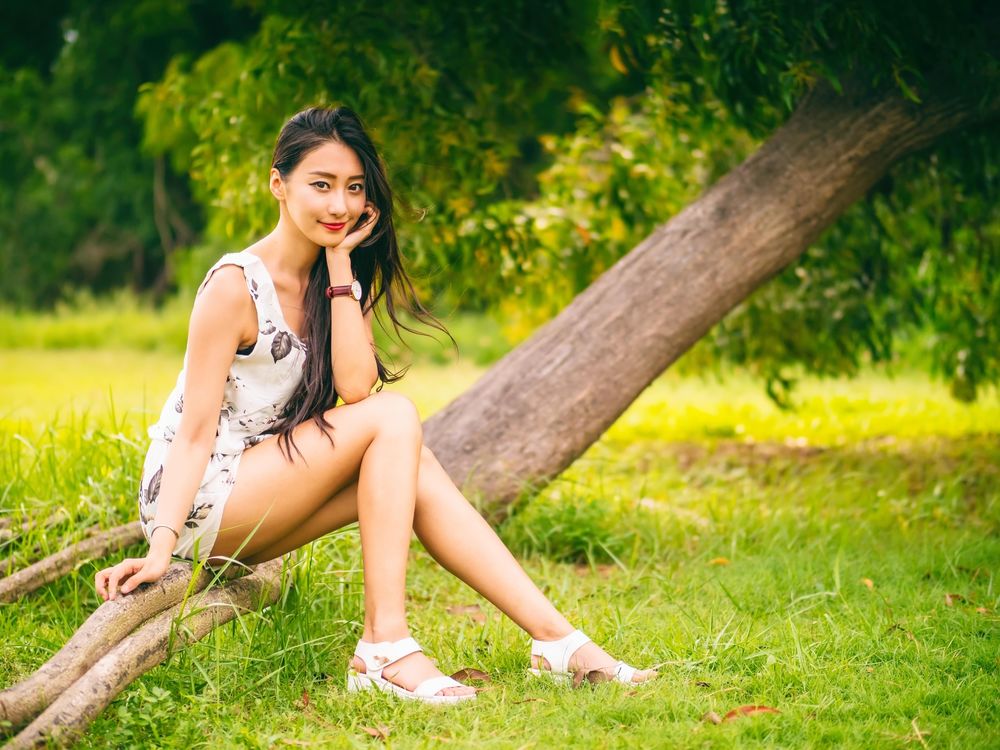 Обои для рабочего стола Девушка азиатка в коротком платье сидит на дереве на фоне природы