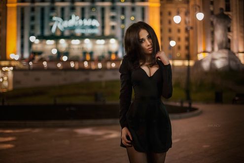 Обои на рабочий стол Девушка в коротком черном платье стоит на площадке на фоне здания в вечерних огнях