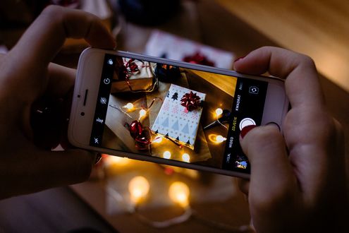 Обои на рабочий стол В руках человека телефон, на который фотографируется новогодний подарок с гирляндой, by freestocks. org