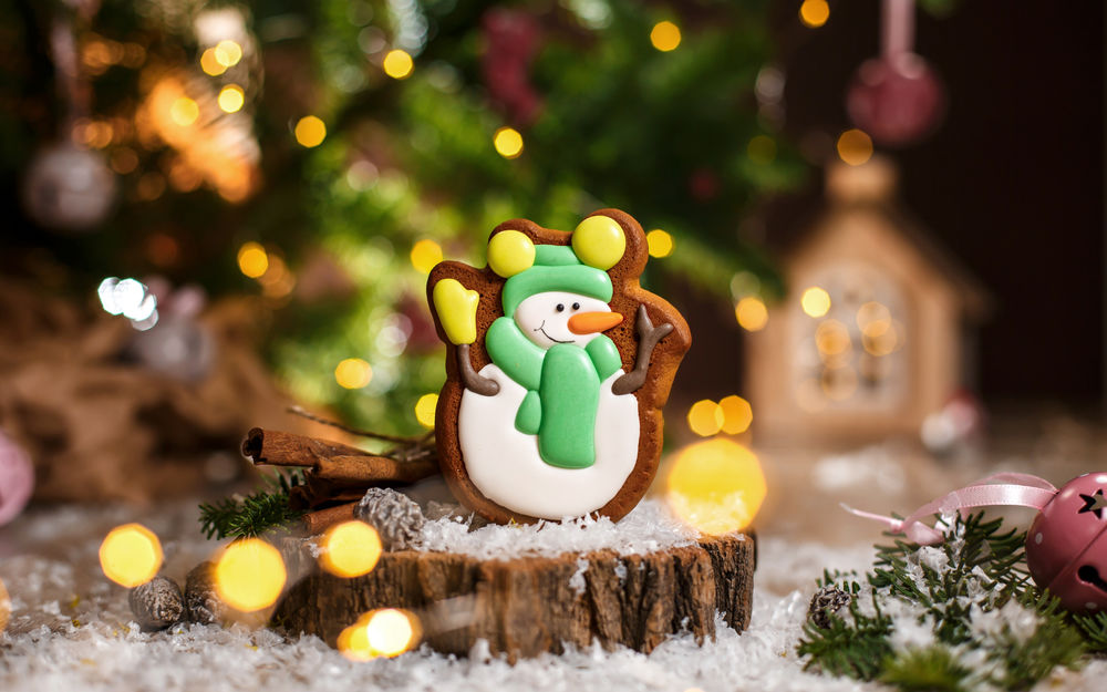Обои для рабочего стола Пряник новогодний в виде снеговика на пеньке с еловыми веточками на размытом фоне