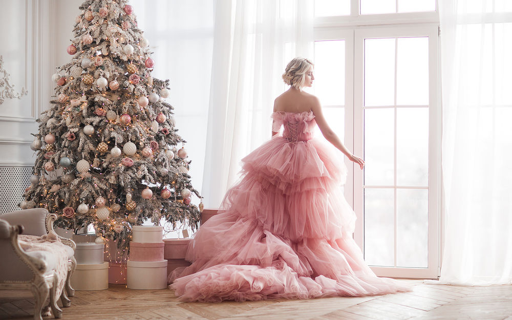 Обои для рабочего стола Блондинка в розовом бальном платье стоит спиной у окна рядом с нарядной новогодней елкой, автор еlenachhil