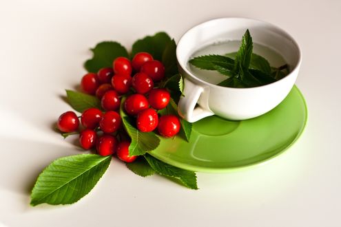 Обои на рабочий стол Чашка с чаем с листочками и вишни рядом