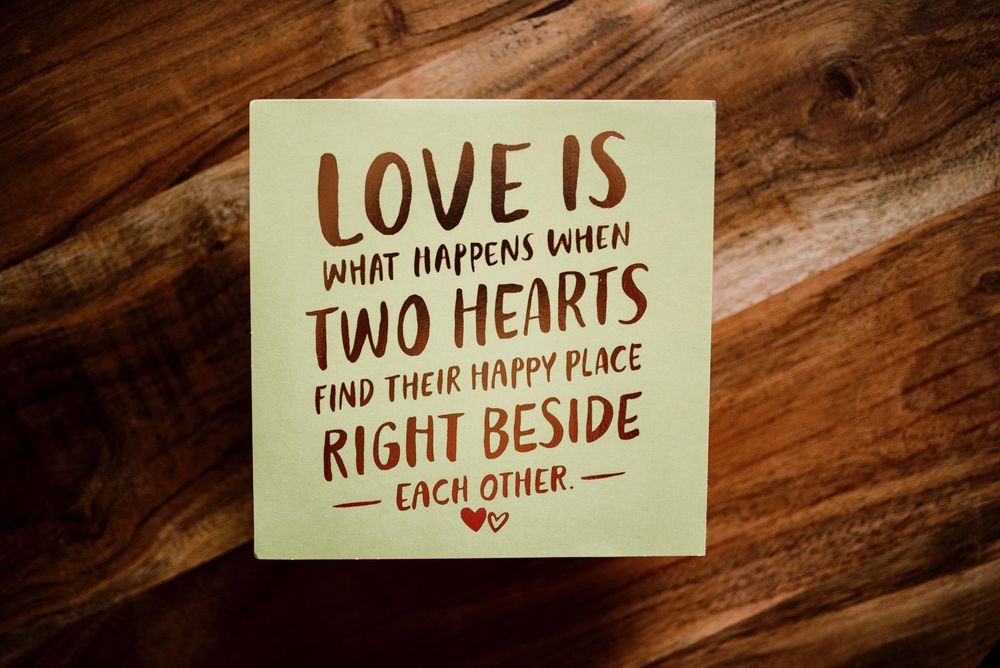 Обои для рабочего стола Записка с текстом LOVE IS WHAT HAPPENS WHEN TWO HEARTS FIND THEIR HAPPY PLACE RIGHT BESIDE EACH OTHER / ЛЮБОВЬ-ЭТО ТО, ЧТО ПРОИСХОДИТ, КОГДА ДВА СЕРДЦА НАХОДЯТ СВОЕ СЧАСТЛИВОЕ МЕСТО РЯДОМ ДРУГ С ДРУГОМ