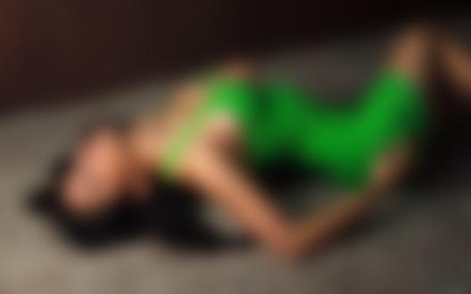Обои на рабочий стол Брюнетка в зеленом обтянутом платье лежит на ковровом покрытии в комнате
