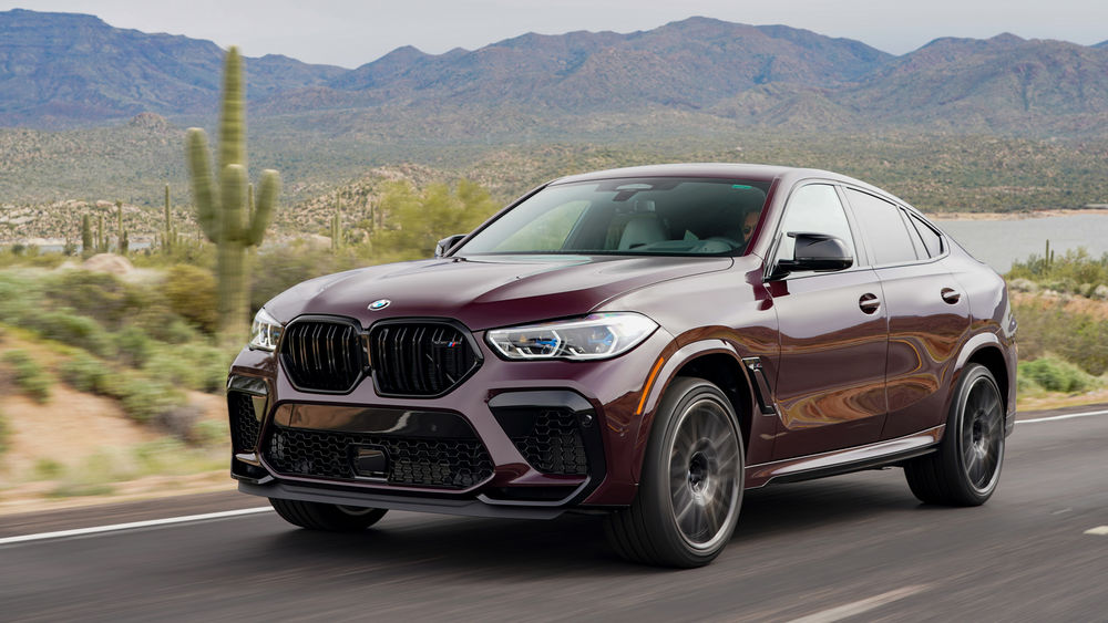 Обои для рабочего стола Мужчина едет за рулем бордового BMW X6 2019 по трассе на фоне гор