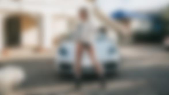 Обои для рабочего стола Блондинка Катрин в короткой пушистой куртке и в черных трусиках стоит на площадке на фоне авто и домов, фотограф Антон Харисов