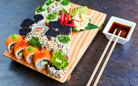 Обои на рабочий стол Японская кухня: ассорти из разных роллов с икрой, васаби и имбирь на подставке. рядом палочки для еды с соусом
