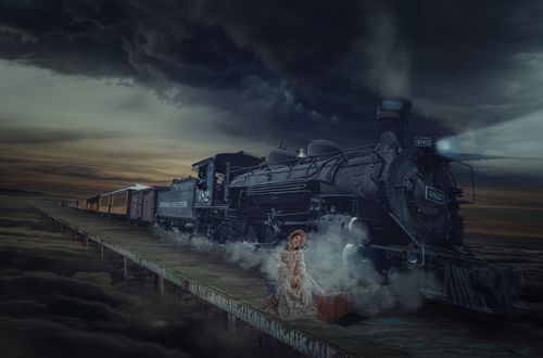 Обои на рабочий стол Девушка в длинном платье и шляпке сидит у поезда на перроне, фотограф Sergii Vidov