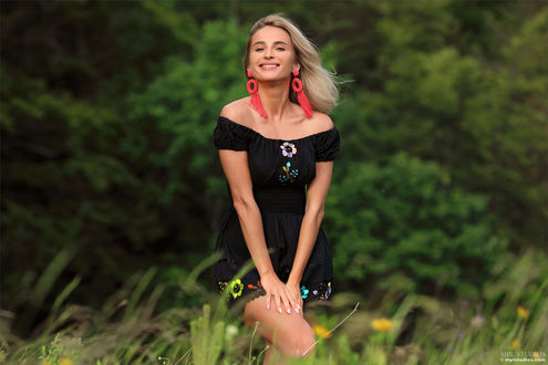 Обои на рабочий стол Блондинка Cara Mell с улыбкой на лице стоит на фоне зелени