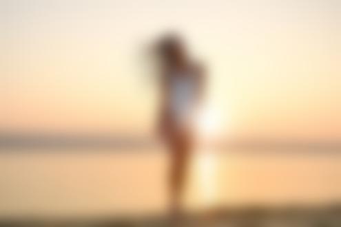 Обои для рабочего стола Девушка с тонким сексуальным телом в белом бикини стоит на пляже на фоне заката. Фотограф Arthur Hidden