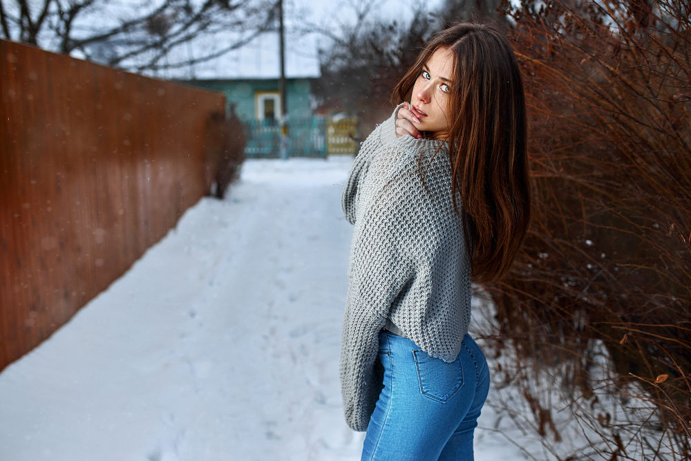 Обои для рабочего стола Девушка в джинсах и свитере стоит на дороге в снегу