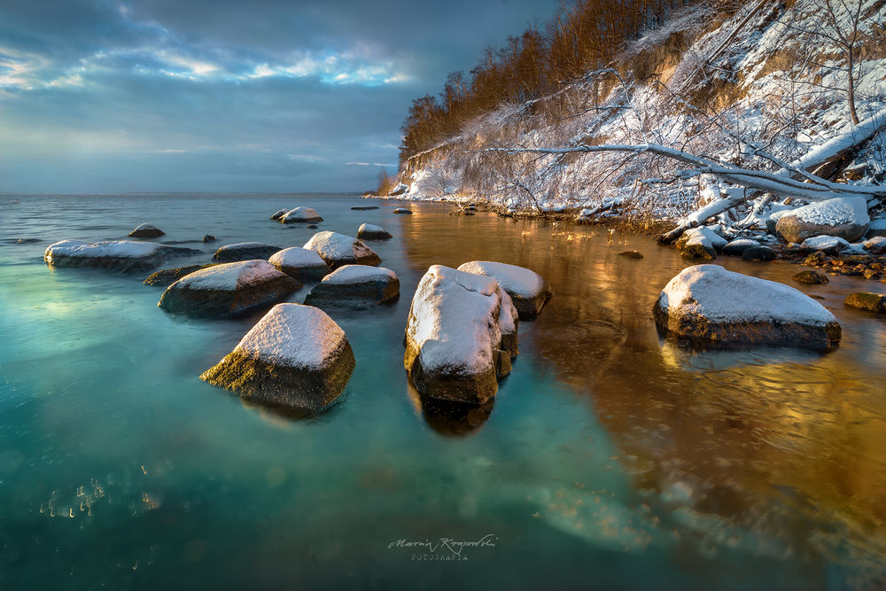 Обои для рабочего стола Камни в снегу в воде у холмистого берега. Фотограф Krasowski Marcin