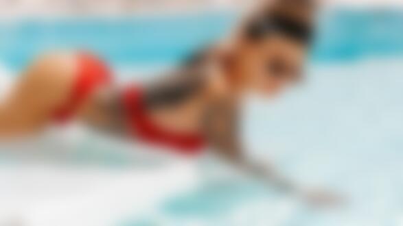 Обои для рабочего стола Девушка с тату в красном купальнике в темных очках стоит на четвереньках в бассейне