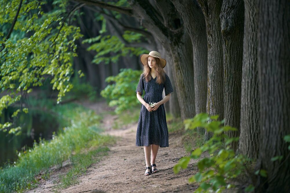 Обои для рабочего стола Девушка Анастасия со шляпой в руке стоит на дорожке с деревьями, фотограф Alexander Vinogradov