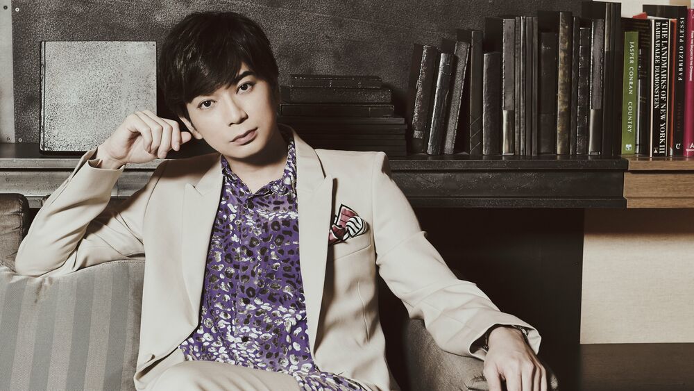 Обои для рабочего стола Певец, актер и телеведущий Мацумото Джун / Matsumoto Jun из группы Араши / Arashi сидит в костюме на диване на фоне полок с книгами