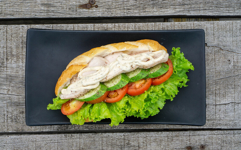 Обои для рабочего стола Вкусная булочка с начинкой из овощей на черной прямоугольной тарелке на досках