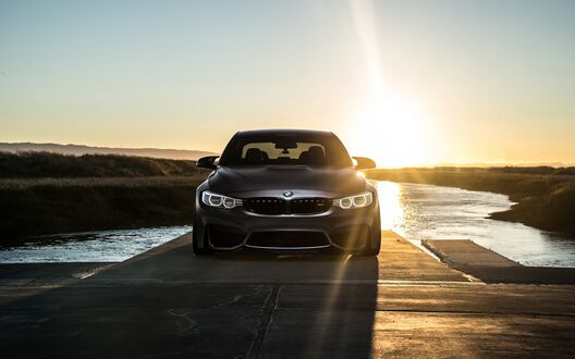Обои на рабочий стол BMW M4 на дороге среди воды на фоне заката