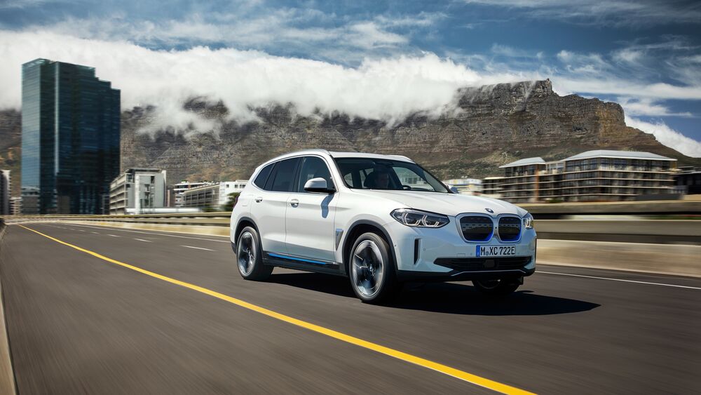 Обои для рабочего стола Электро автомобиль белого цвета BMW IX3 мчится по дороге