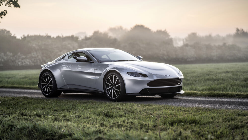 Обои для рабочего стола Серебристый Aston Martin стиот на проселочной дороге возле леса