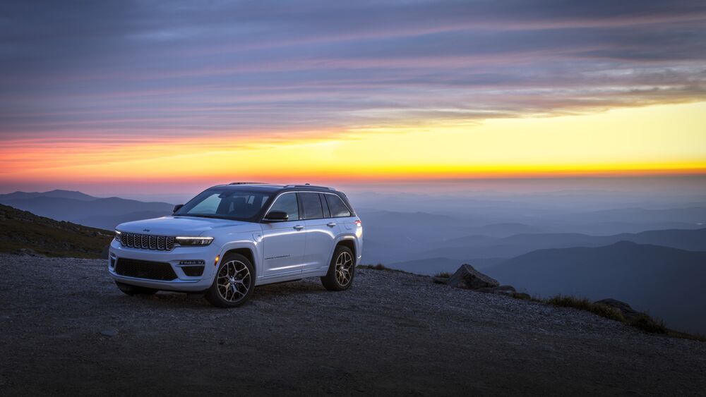 Обои для рабочего стола Внедорожник белого цвета Джип / Jeep Grand Cherokee Summit Reserve 4xe (WL) стоит на вершине горы на фоне закатного неба